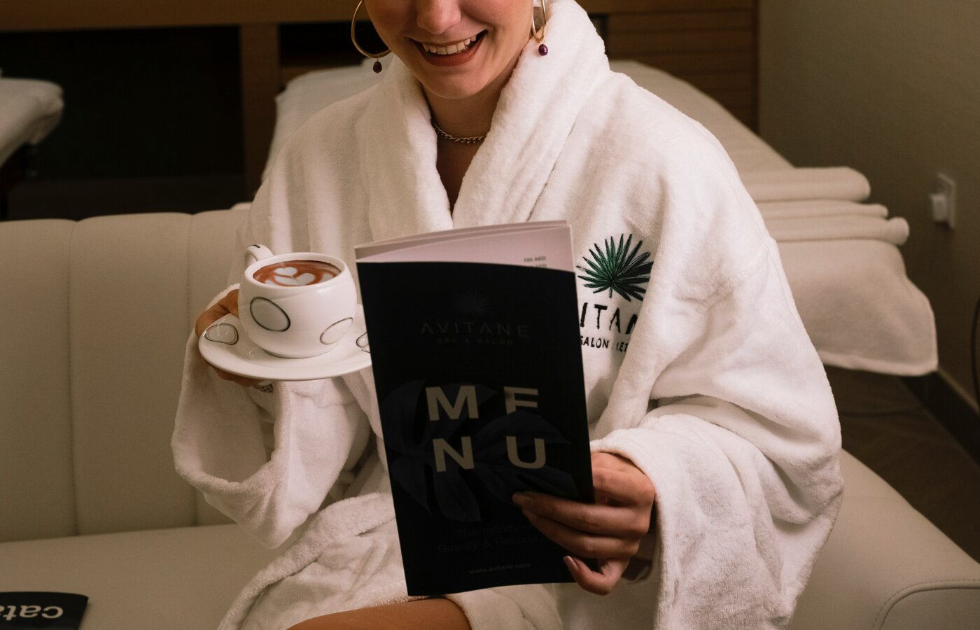 A beauty therapist in a plain navy side-fastening tunic preparing a treatment room with folded white towels