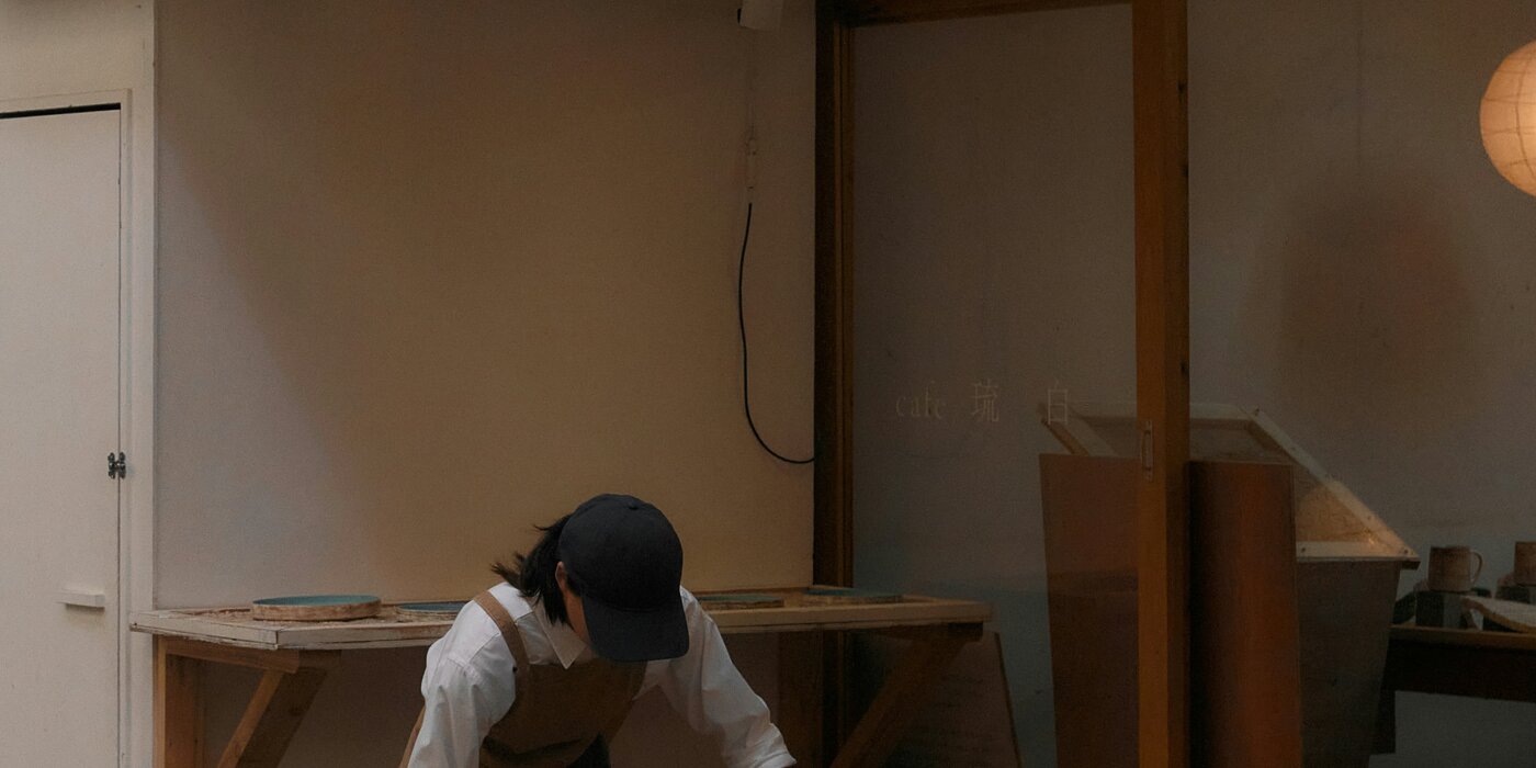 A tradesperson kneeling on a timber floor in grey work trousers, with a tool pouch and hammer beside them