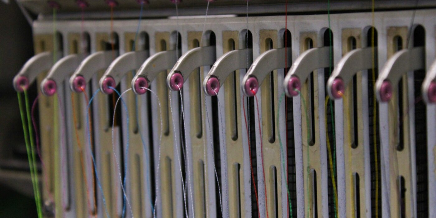 Close-up of an industrial embroidery machine stitching a simple abstract emblem onto a navy polo shirt